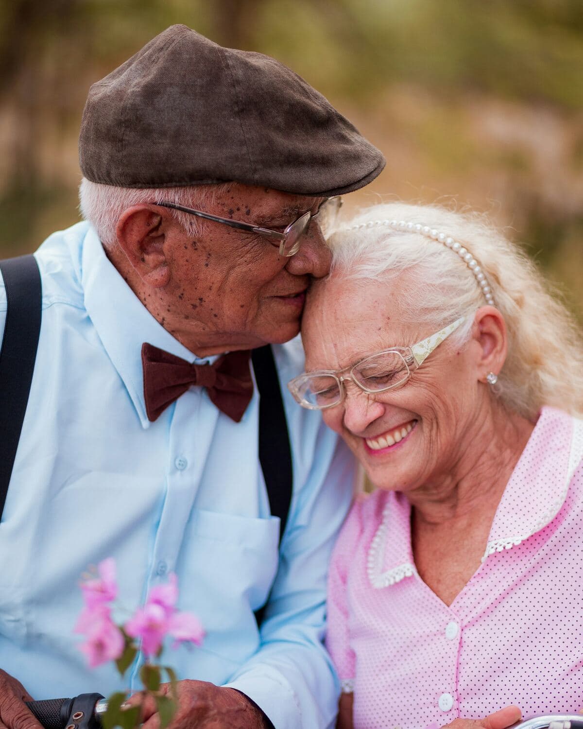 Una pareja de adultos mayores sonríe abrazada entre flores