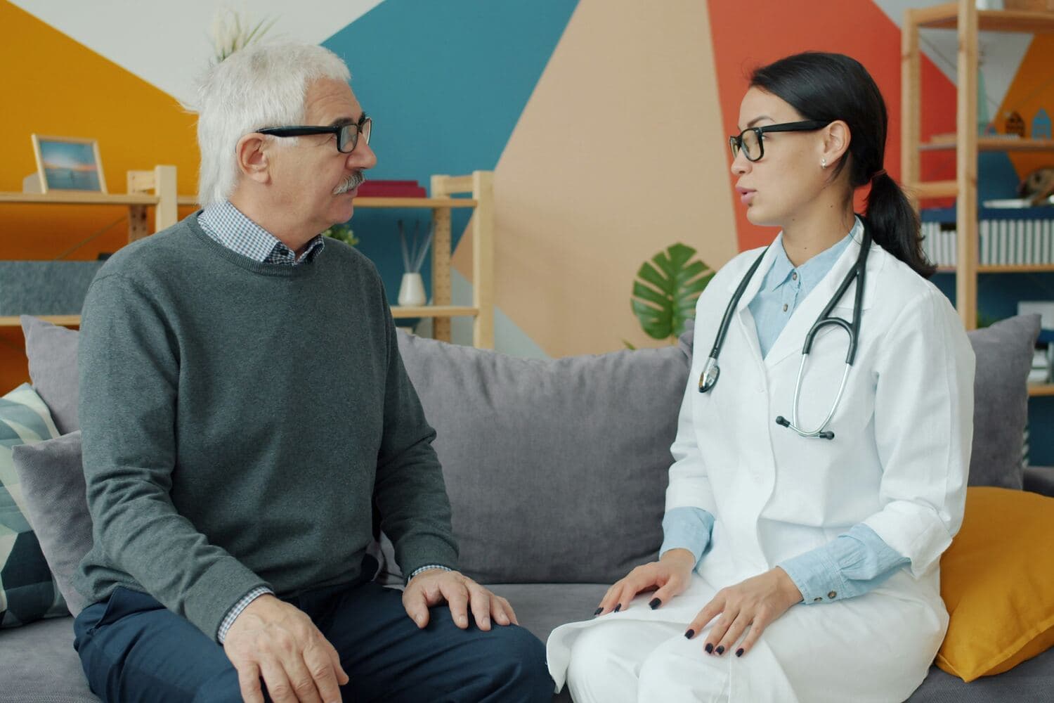 Una doctora conversa con un señor mayor, los dos sentados en un sofá