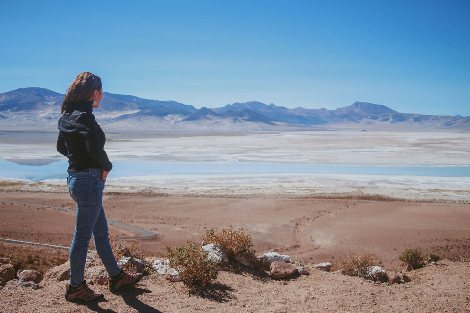 Una mujer mira una planicie de sal con montañas al fondo
