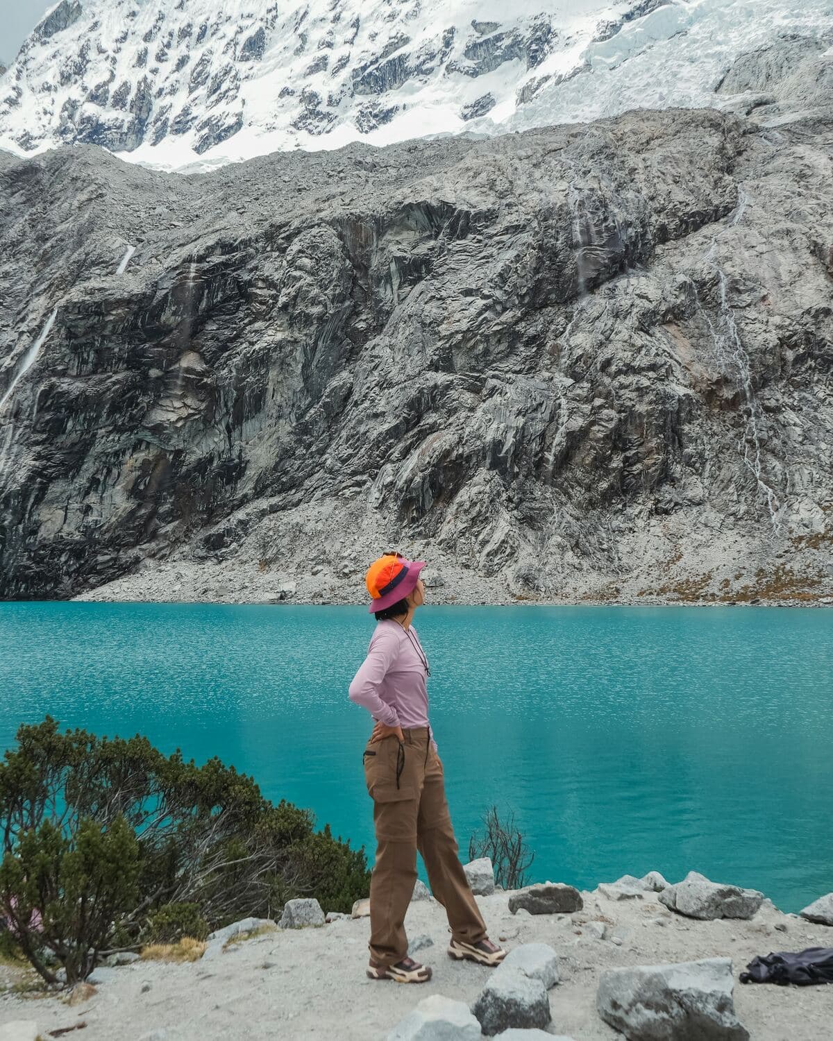 Una mujer contempla una laguna turquesa al pie de una montaña nevada