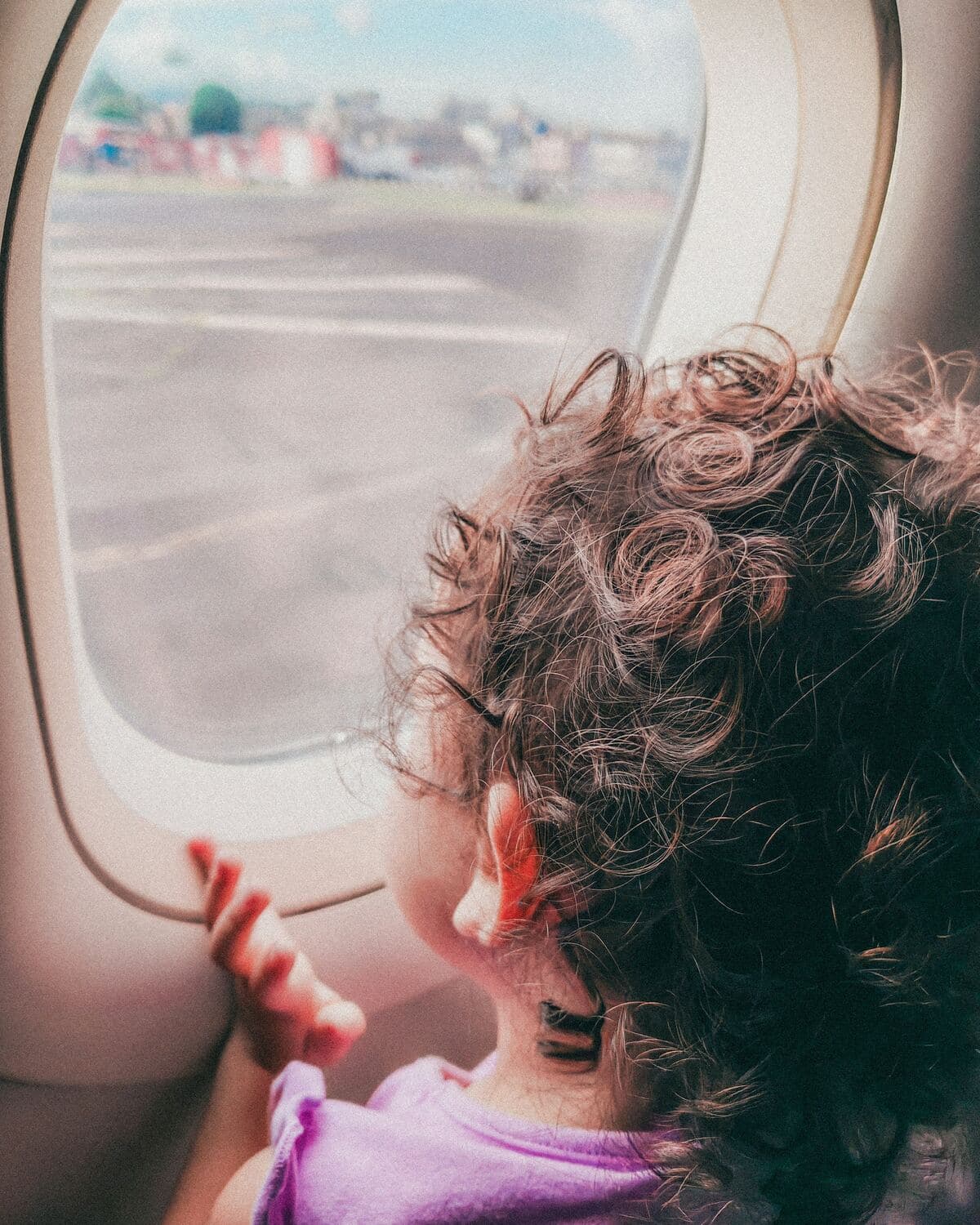 Una niña pequeña de pelo rizado mira por la ventanilla de un avión antes de despegar