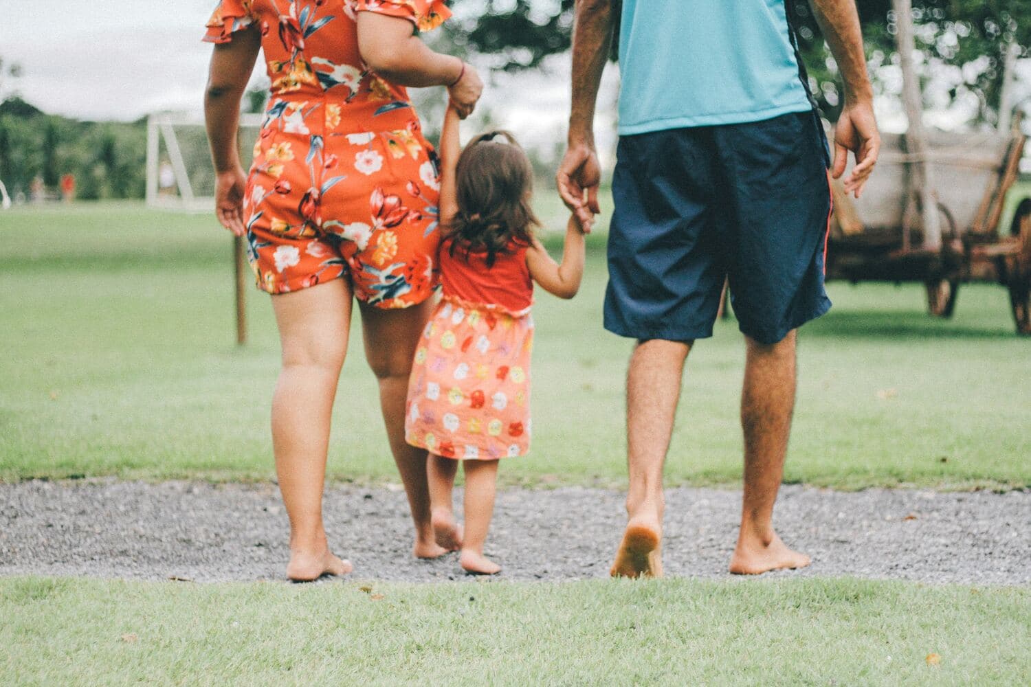 Una mamá, un papá y su hija caminan descalzos de la mano sobre el pasto